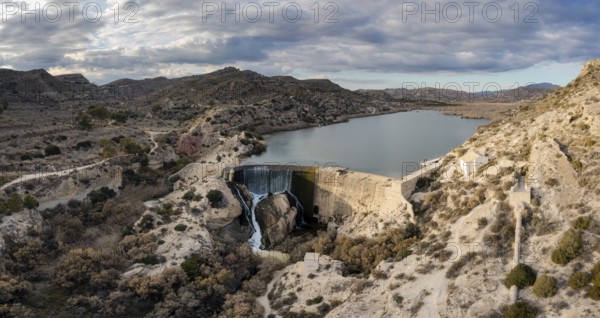 A drone view of the Elche Reservoir and dam wall with waterfall and surrounding semi-desert