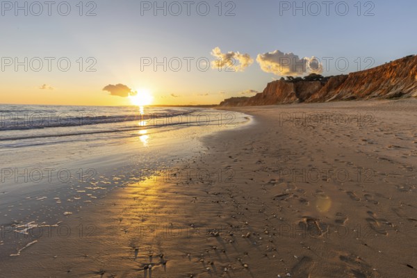 Beautiful sandy beach with red rocks and cliffs. Twilight at sunset with shallow waves on the
