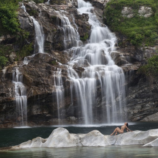 Professional model in elegant pose on a rocky island in front of an impressive waterfall, Aesthetic
