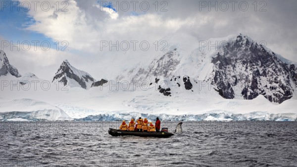 Group in a boat in the foreground, surrounded by snow-covered mountains and overcast sky, people in