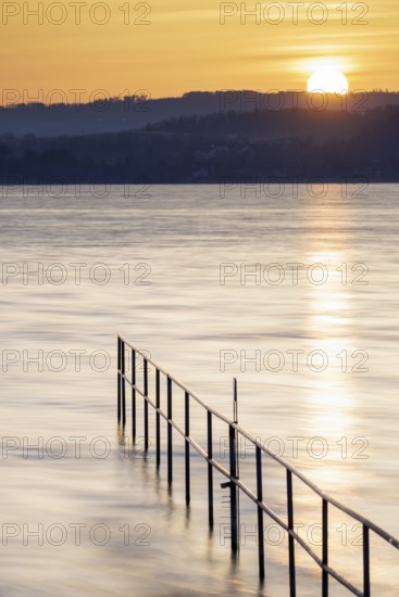 Rising sun over calm lake, railing extends into the water, lido, Litzelstetten, Lake Constance,