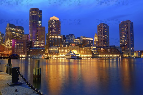 Boston\'s skyline glows at sunset, reflecting off the water at Fan Pier.