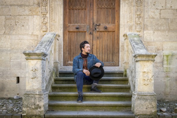 Portrait of a young man sitting against a beautiful old medieval cathedral door. A man in front of