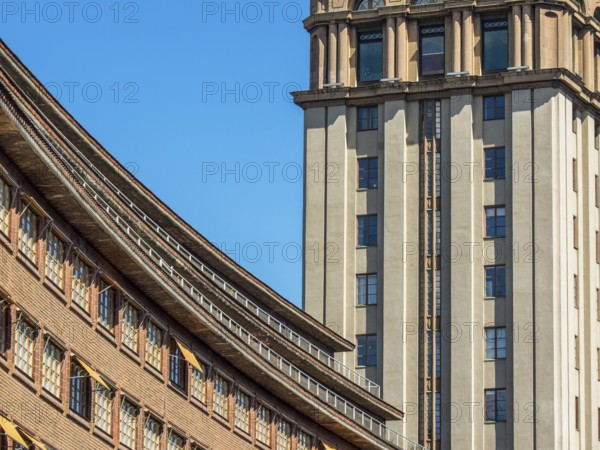 Modern building with a striking facade and a skyscraper in the background under a clear blue sky,