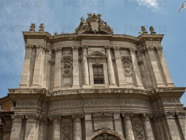 Front façade of a baroque building with intricate ornamentation and Latin inscription, framed in a