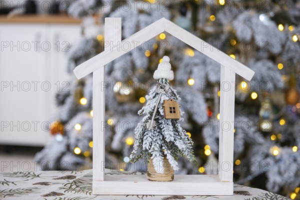 Key on Christmas tree and tiny house on cozy home with Christmas decor on table of festive white