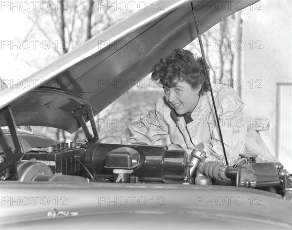 In the 1950s. A woman in an overall fixing something on the car that has it's hood open. Sweden