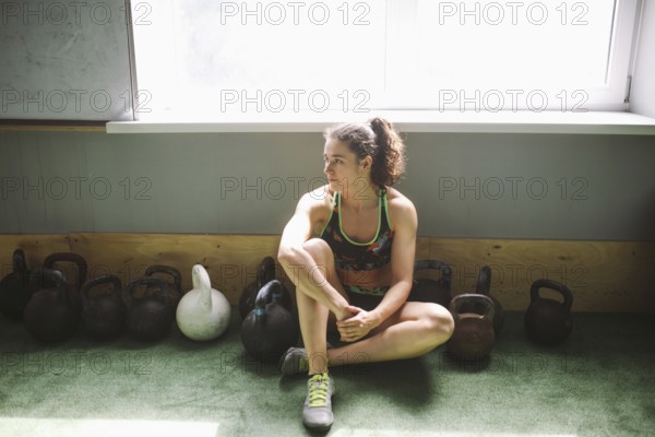 The girl is resting, taking a break during training in the gym. Sits by the window near a lot of