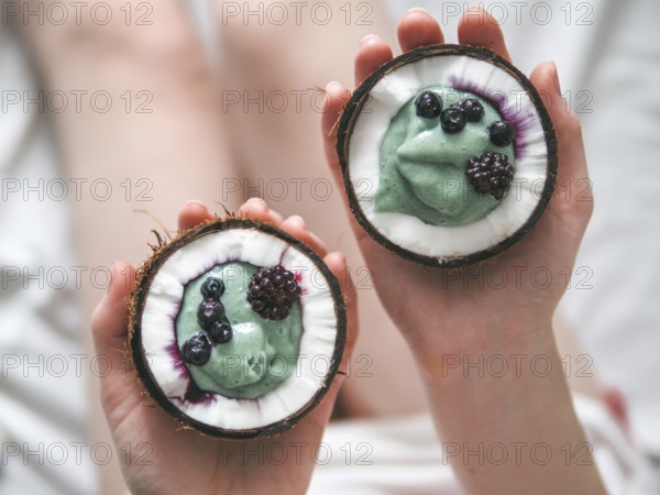 Two coconut half with smoothie or yogurt in woman hands. Blue spirulina smoothie in coconut with