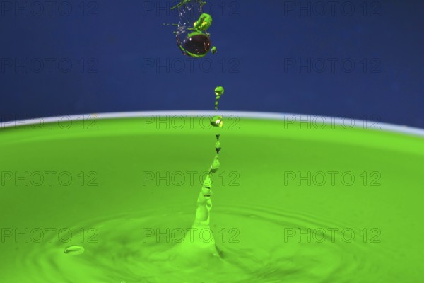 Green liquid splashes in a dynamic moment against a blue background, water droplets, collision,