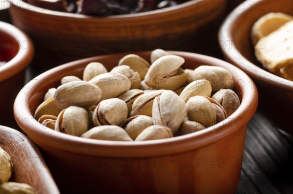 Pistachio nuts in clay bowl on kitchen wooden table food background