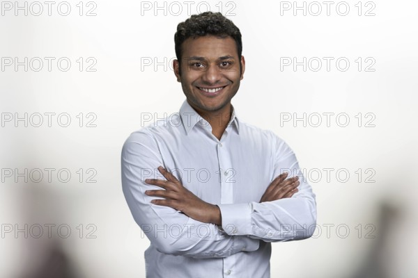 Handsome smiling man with crossed arms looking at camera. Portrait of indian businessman on blurred
