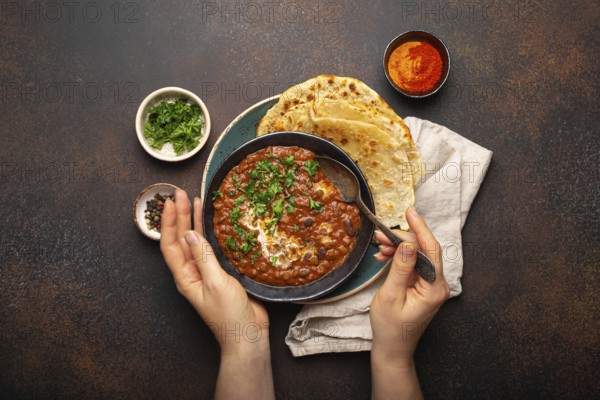 Female hands holding a bowl and eating traditional Indian Punjabi dish Dal makhani with lentils and