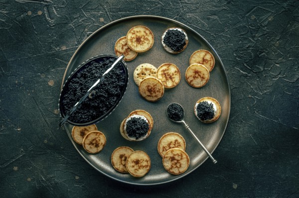 Blinis with black caviar and cream cheese, overhead flat lay shot on a black background, mini