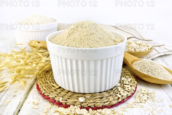 Oat flour in white bowl, oatmeal and bran in a spoon, stalks of oats, napkin against the background