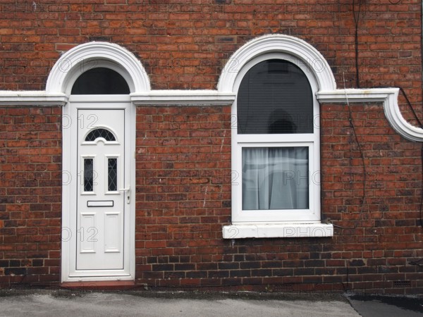 White front door and window of a typical old brick british terraced house with white decorative