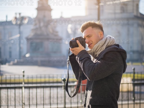 Handsome young male photographer taking photograph with professional photo camera hanging from his