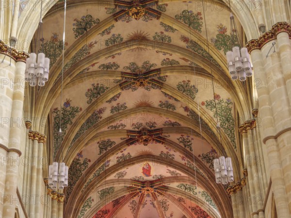 The interior of a church with ornate frescoes on the vaulted ceiling and decorative Gothic style