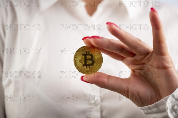 Virtual cryptocurrency money Bitcoin golden coin in the left hand of a woman with red nail polish.