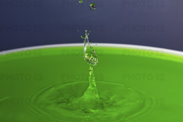 A drop of water forms a splashing sculpture on green liquid, water droplets, collision, high-speed