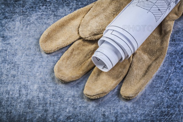 Rolled up engineering drawings leather protective gloves on metallic background construction