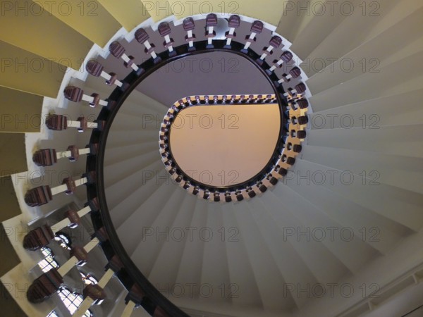 A looking upwards view of an elegant spiral staircase with wooden bannisters in elegant shades of