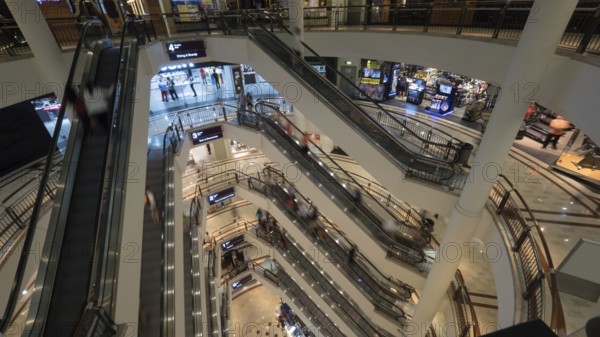Customers in trade centre riding escalators. View from upper to lower floor. Shopping mall of