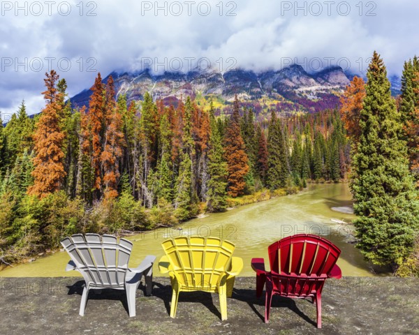 Scenic autumn in the Rockies of Canada. Three deck chairs stand over the forest and river.