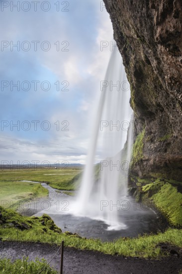 Sunny day in Iceland. Seljalandsfoss waterfall in July. Large rainbow decorates a drop of water.