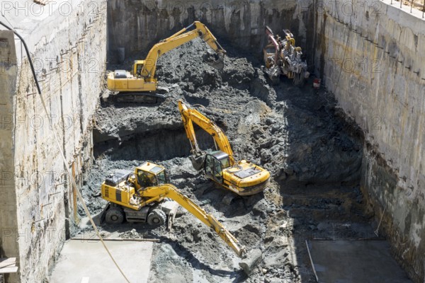 Excavators dig at a construction site of a street and a subway. Baggers transport dirt to a higher