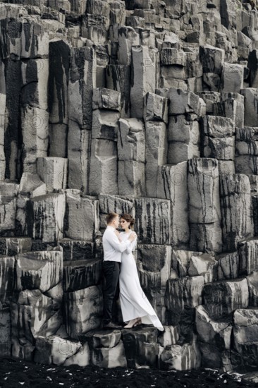 A wedding couple stands on a wall of stone pillars. The bride and groom are hugging on basalt