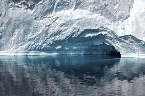 A large iceberg with a small cave is reflected in the calm, reflective water, icebergs in the