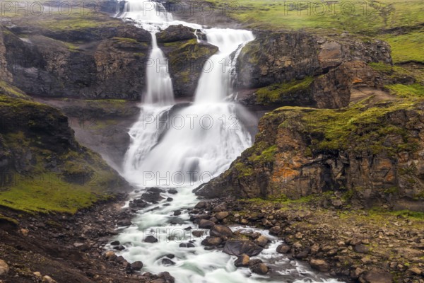 Powerful streams of cascade falls with a roar break against cold rocks. Cold and rainy July in