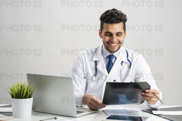 Handsome doctor looking at x-ray scan. Happy physician in white coat with stethoscope sitting at