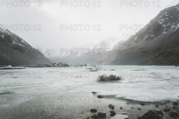 Mountain valley with frozen lake, surrounded by snow-capped mountains under a cloudy sky, Hooker