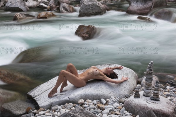A woman in an elegantly professional pose on a rock, framed by flowing water, with pebbles stacked
