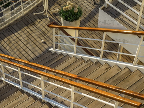 Wooden staircase with railing on a ship deck and a decorative potted plant with flowers, stockholm,