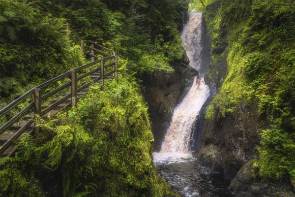 Spectacular wooden boardwalk on the hill with a view on tall waterfall and river in majestic