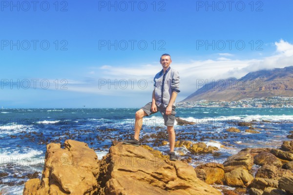 Male model tourist traveler at False Bay rough coast landscape with boulders waves and mountains