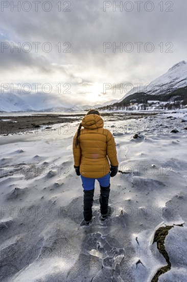 A woman in winter clothing on the frozen shore of the Ullsfjord, Sjursnes, Tromso, Troms, Norway,