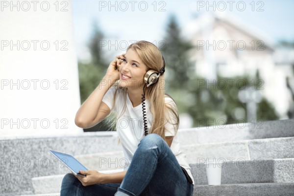 Happy young woman with vintage headphones and a cup of coffee to go, surfing the internet on a