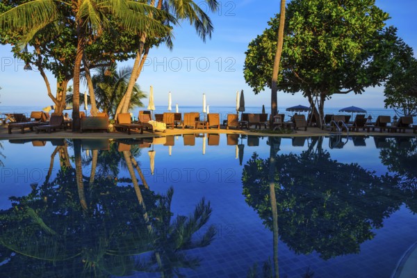Sunset on the beach resort. An oceanfront pool surrounded by palm trees. Palm trees reflected in