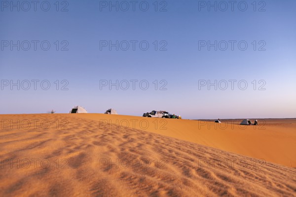 Tents and cars standing on a sand dune in the desert under a wide sky at sunset, camping in the