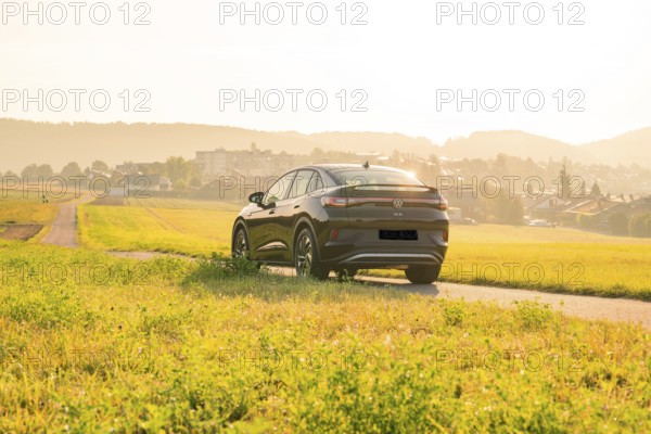 SUV driving on a country road with a view of a town at sunset, VW ID5 electric car, Calw, Black