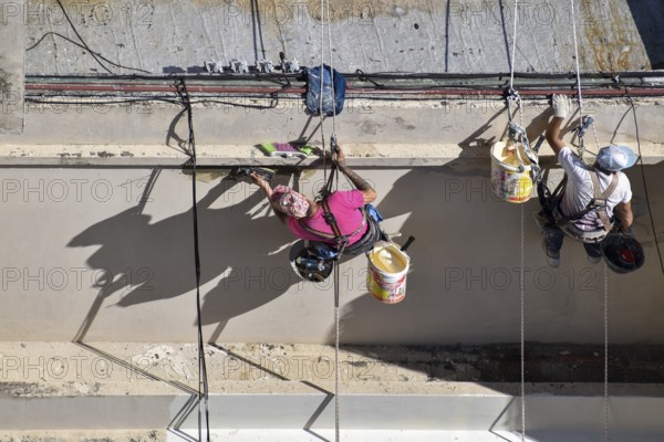 Painter hanging from a rope while working on a façade, symbolic image for safety in construction,