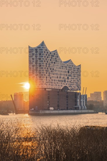 The sun rises behind the Elbphilharmonie and illuminates the surrounding area in golden colours,