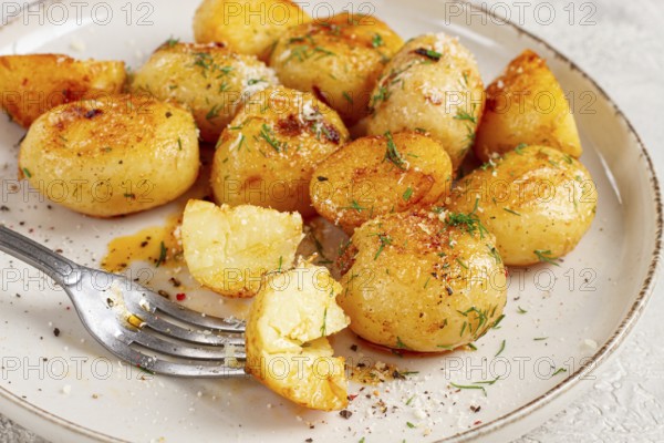 Half-eaten fried new potatoes, with butter and dill, on a white plate, with a fork, at home, no