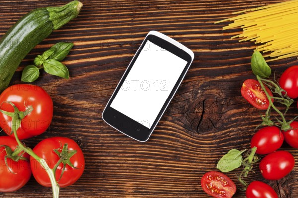 Fresh vegetables and pasta on wooden table with smartphone and recipe on screen. Groceries, recipe