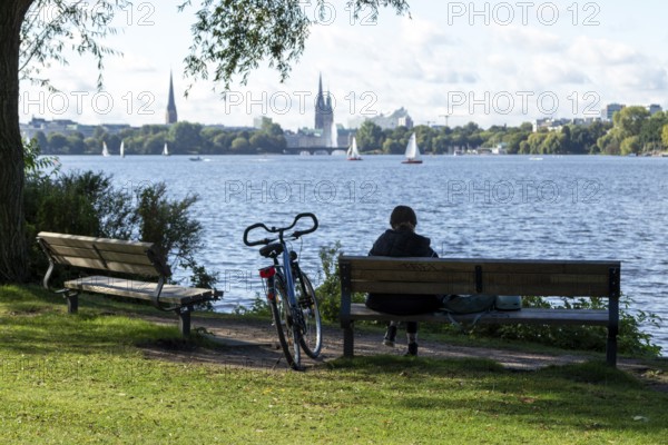 Leisure activities in summer, bicycle and woman on park bench, behind them sailing boats in front