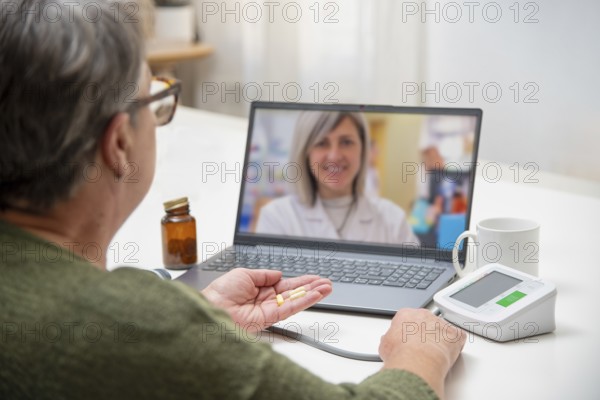 Senior woman having online medical consultation with doctor using laptop, holding pills in hand and